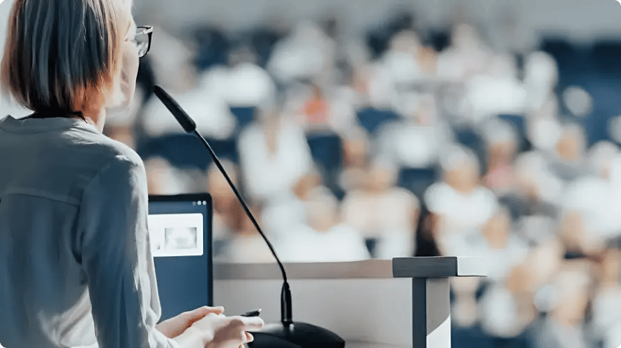 Speaker at a lectern addressing a full conference audience, an event supported by InHouse Physicians.